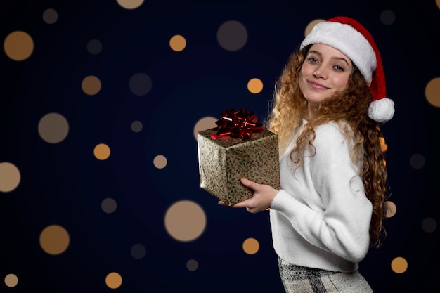 Young latin woman showing a christmas present with a santa claus hat. space for text.