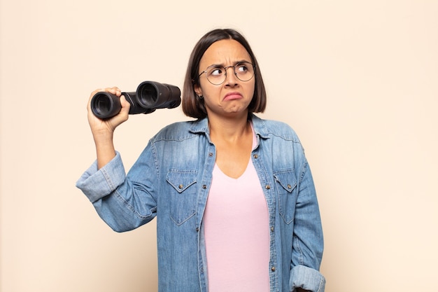 Young latin woman shrugging, feeling confused and uncertain, doubting with arms crossed and puzzled look