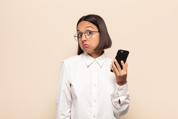 young latin woman shrugging, feeling confused and uncertain, doubting with arms crossed and puzzled look