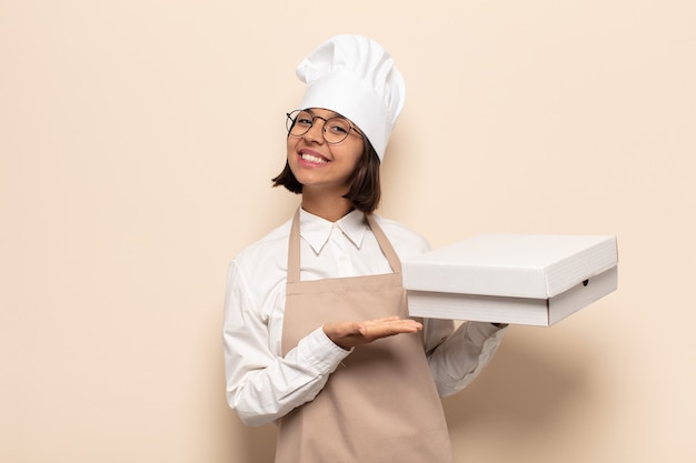 Young latin woman smiling cheerfully, feeling happy and pointing to the side and upwards, showing object in copy space