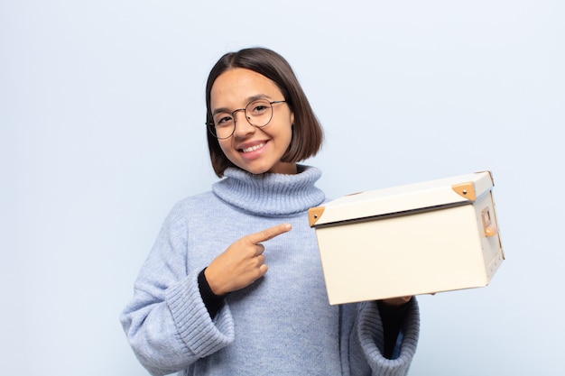 Young latin woman smiling cheerfully, feeling happy and pointing to the side and upwards, showing object in copy space