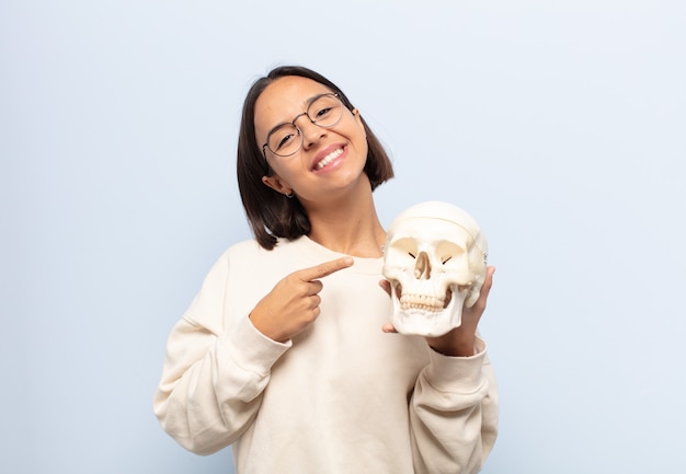 Young latin woman smiling cheerfully, feeling happy and pointing to the side and upwards, showing object in copy space