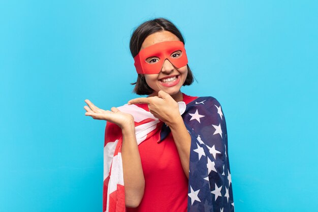 Young latin woman smiling cheerfully and pointing to copy space on palm on the side, showing or advertising an object