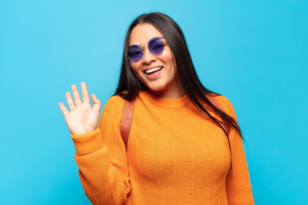 Foto giovane donna latina che sorride allegramente e allegramente, agitando la mano, dandoti il benvenuto e salutandoti o salutandoti