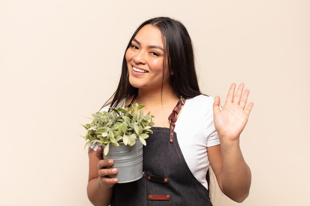 Young latin woman smiling happily and cheerfully, waving hand, welcoming and greeting you, or saying goodbye