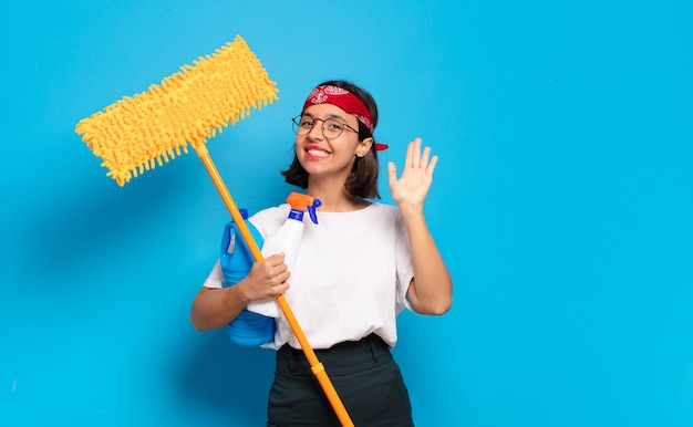 Young latin woman smiling happily and cheerfully, waving hand, welcoming and greeting you, or saying goodbye