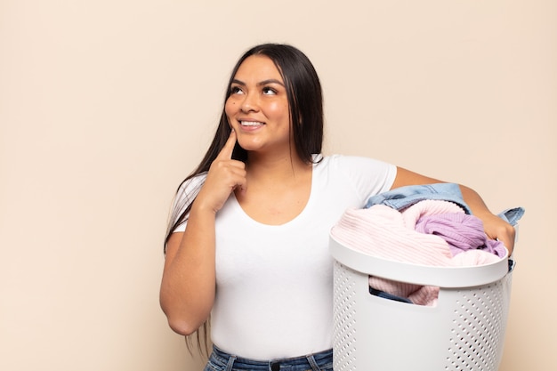 Young latin woman smiling happily and daydreaming or doubting, looking to the side