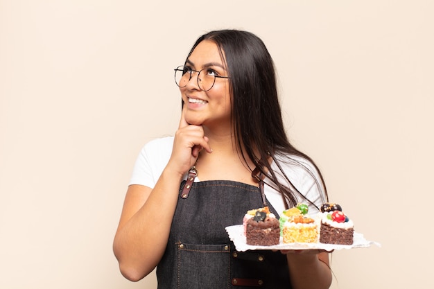 Young latin woman smiling happily and daydreaming or doubting, looking to the side