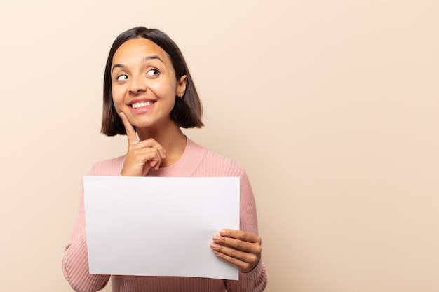 Young latin woman smiling happily and daydreaming or doubting, looking to the side