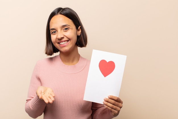 Young latin woman smiling happily with friendly, confident, positive look, offering and showing an object or concept