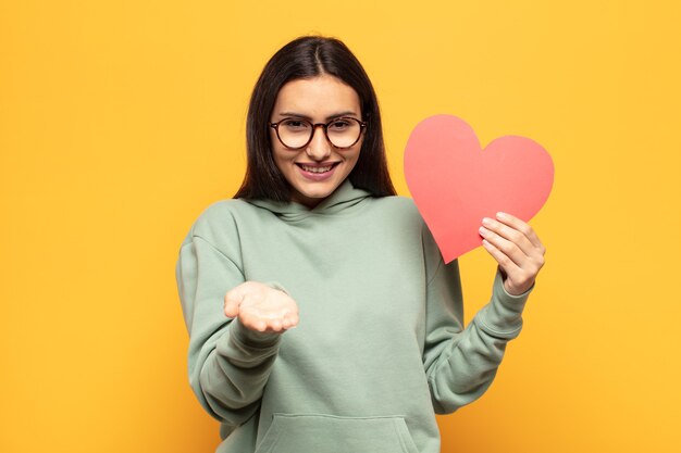 Giovane donna latina che sorride felicemente con uno sguardo amichevole, fiducioso e positivo, offrendo e mostrando un oggetto o un concetto