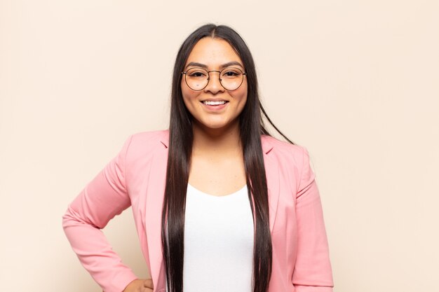 Young latin woman smiling happily with a hand on hip and confident, positive, proud and friendly attitude