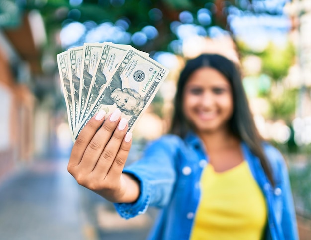 Young latin woman smiling happy holding usa dollars banknotes at city.