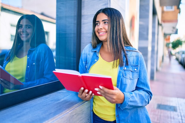 Young latin woman smiling happy reading book at city.