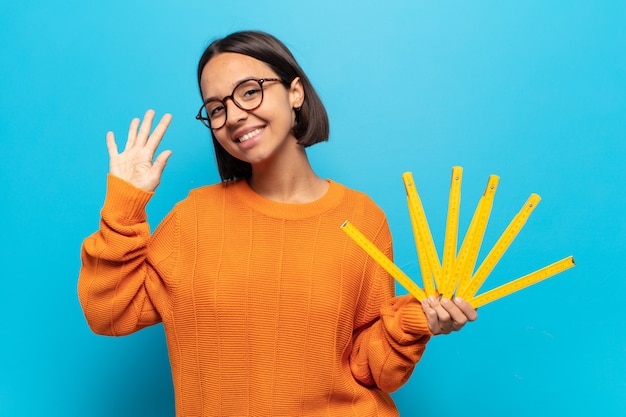 Young latin woman smiling and looking friendly, showing number five or fifth with hand forward, counting down