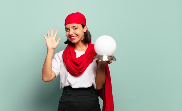 Young latin woman smiling and looking friendly, showing number five or fifth with hand forward, counting down