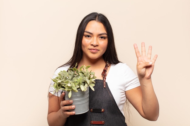 Young latin woman smiling and looking friendly, showing number four or fourth with hand forward