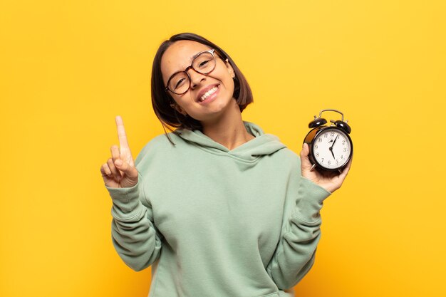 Young latin woman smiling and looking friendly, showing number one or first with hand forward, counting down