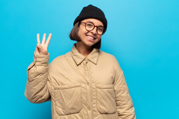 Young latin woman smiling and looking friendly, showing number three or third with hand forward, counting down