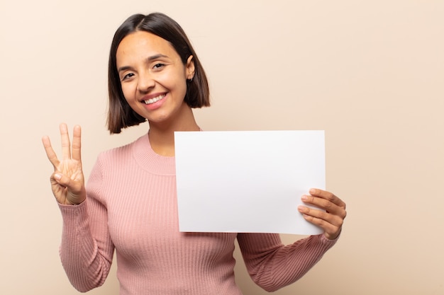 Young latin woman smiling and looking friendly, showing number three or third with hand forward, counting down