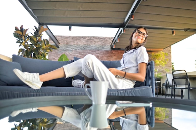 Young latin woman smiling sitting on a sofa with a cup of coffee at sunset