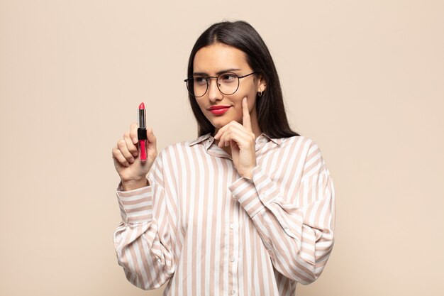 Young latin woman smiling with a happy, confident expression with hand on chin, wondering and looking to the side