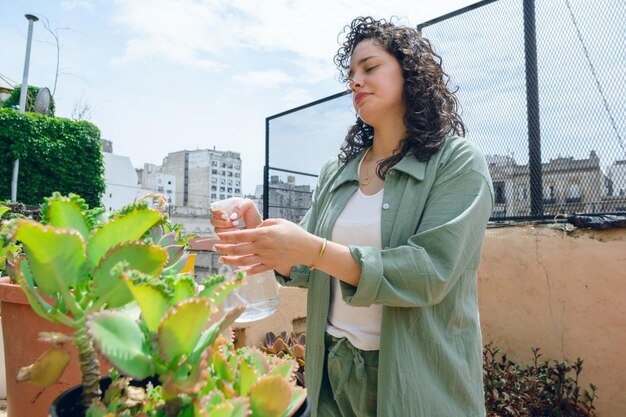 Photo young latin woman standing with water sprayer wetting plants in terrace garden