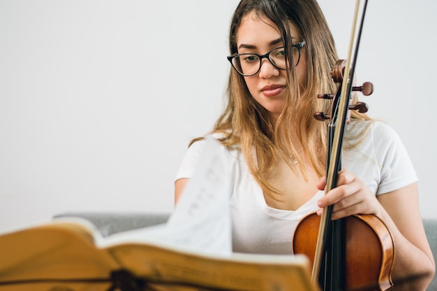 彼女の手でバイオリンと座って楽譜を勉強している自宅で若いラテン女性バイオリニスト