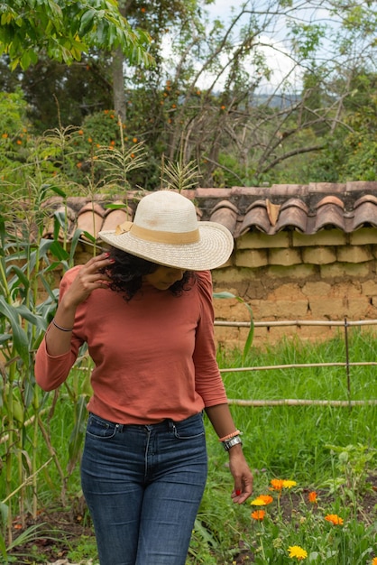 彼女の野菜の庭の薬用花をチェックする帽子をかぶっている若いラテン女性