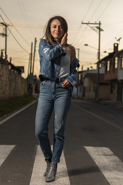 Young latin woman wearing blue jeans and jean jacket walking over pedestrian zebra crosswalk selective focus