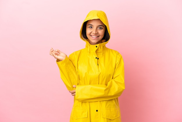 孤立した背景の上に防雨コートを着て、来るように誘うために手を横に伸ばしている若いラテン女性