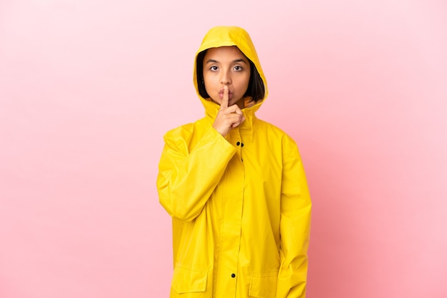 Young latin woman wearing a rainproof coat over isolated background showing a sign of silence gesture putting finger in mouth