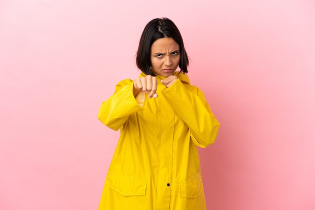 Young latin woman wearing a rainproof coat over isolated background with fighting gesture