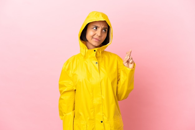 Photo young latin woman wearing a rainproof coat over isolated background with fingers crossing and wishing the best