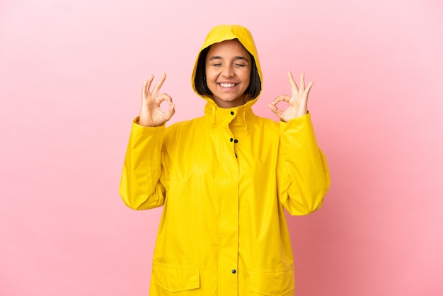 禅のポーズで孤立した背景の上に防雨コートを着ている若いラテン女性