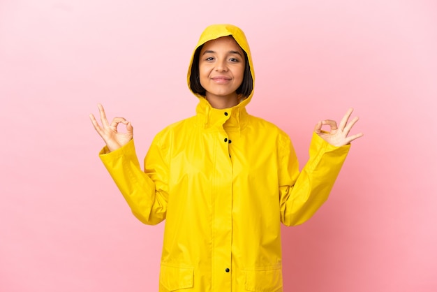 禅のポーズで孤立した背景の上に防雨コートを着ている若いラテン女性