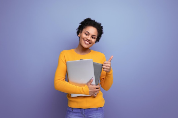 Giovane donna latina con i capelli afro che tiene un computer portatile per studiare nelle sue mani su uno sfondo di studio