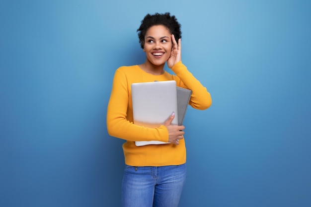 Foto giovane donna latina con i capelli afro che tiene un portatile per studiare nelle sue mani sullo sfondo di uno studio