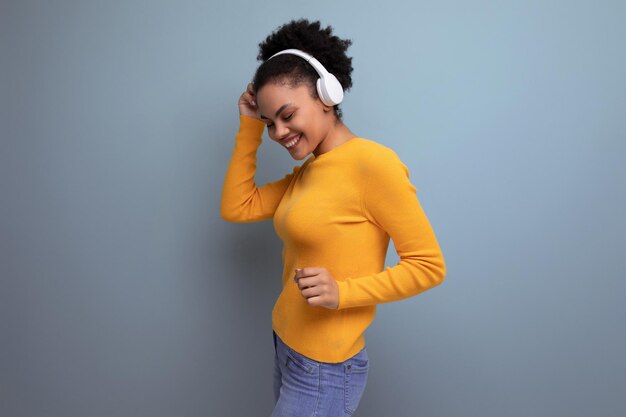 Foto giovane donna latina con capelli afro che ascolta musica con le cuffie sullo sfondo dello studio