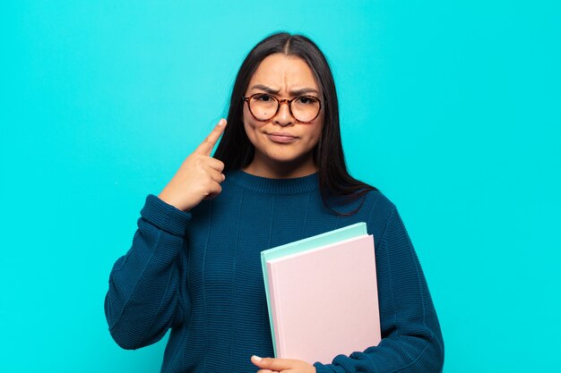 Young latin woman with a bad attitude looking proud and aggressive, pointing upwards or making fun sign with hands