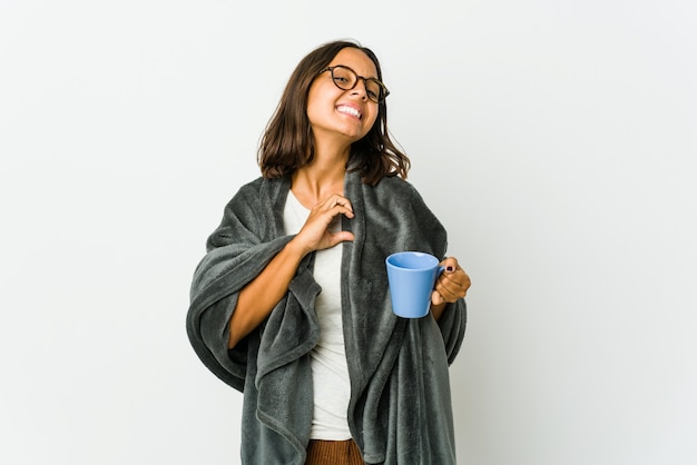 Young latin woman with blanket isolated on white background smiling and showing a heart shape with hands.