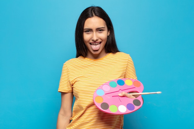 Young latin woman with cheerful, carefree, rebellious attitude, joking and sticking tongue out, having fun