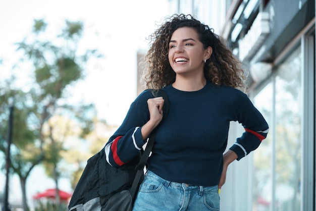 Young latin woman with curly hair smiling while walking outdoors on the street. Urban concept.