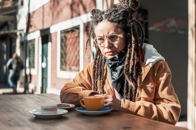 コーヒーを飲みながらカフェテリアの外に座っているドレッドヘアを持つ若いラテン女性