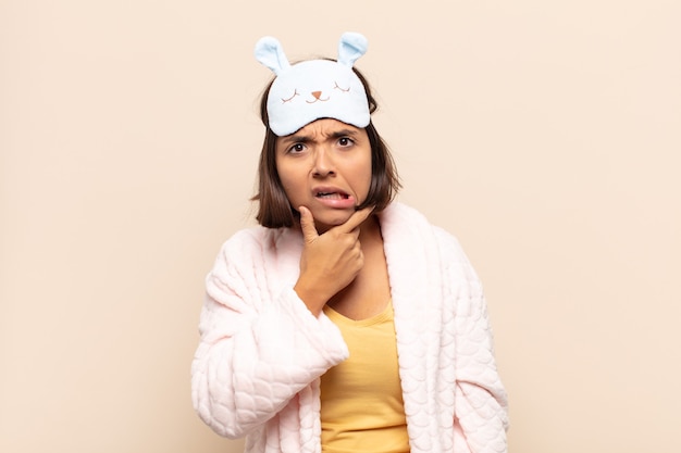 Young latin woman with mouth and eyes wide open and hand on chin, feeling unpleasantly shocked