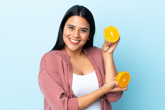 Young latin woman woman isolated on blue holding an orange