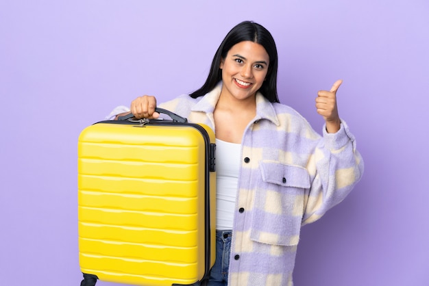 Young latin woman woman isolated on purple in vacation with travel suitcase and with thumb up