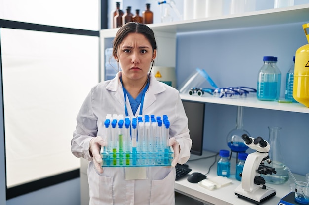 Young latin woman working at scientist laboratory skeptic and nervous, frowning upset because of problem. negative person.