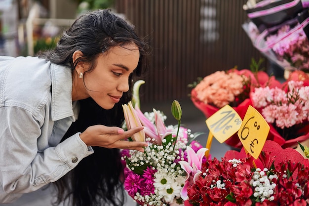 Giovane donna latina che si diletta nella bellezza profumata dei fiori colorati alla bancarella di un venditore ambulante