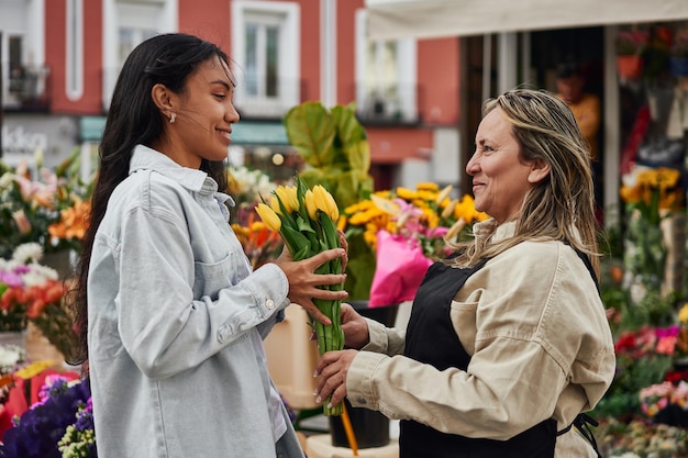 정원사가 건네주는 노점상 가판대에서 활기찬 꽃을 구입하는 젊은 라티나 여성